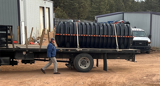 A truck trailer holds a septic tank. A man walks beside the trailer.