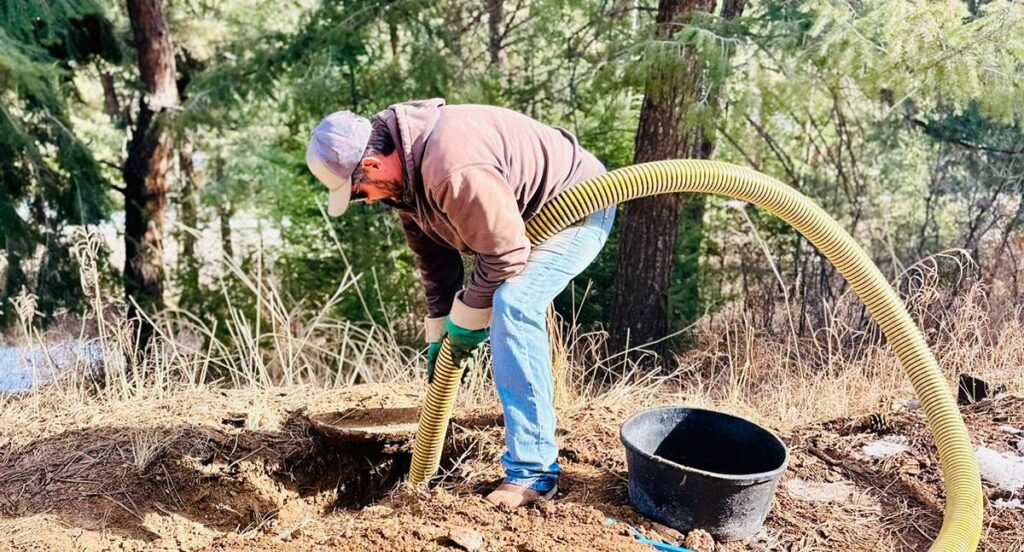 A man uses a large hose while working on an underground septic tank.