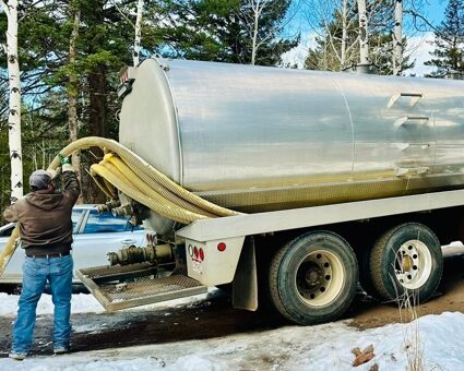 A silver and yellow septic maintenance truck. A worker is pulling a hose off the back of the truck.