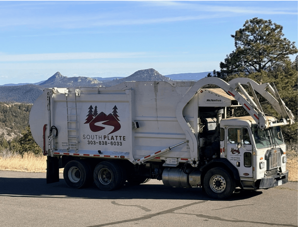 A white South Platte Services, LLC trash truck parked in front of a view of the Conifer and Bailey landscape.