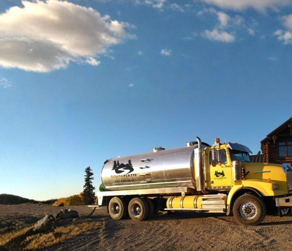 A yellow South Platte Services, LLC tanker truck with a silver tank umping a septic tank.