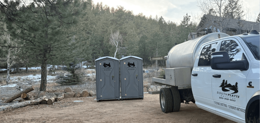 A pair of South Platte Services, LLC portable toilets (porta-potties) sit at a trailhead next to a cleanup truck.
