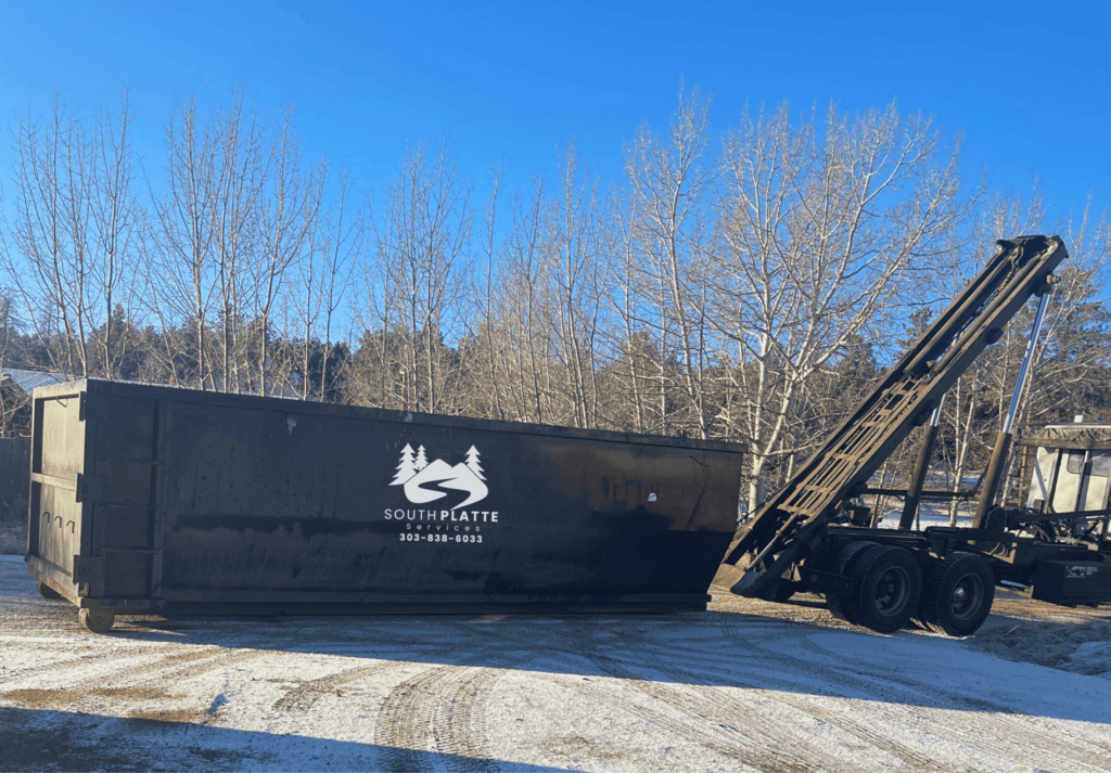 A South Platte Services truck unloads a roll-off dumpster on a snowy driveway in Evergreen, CO.