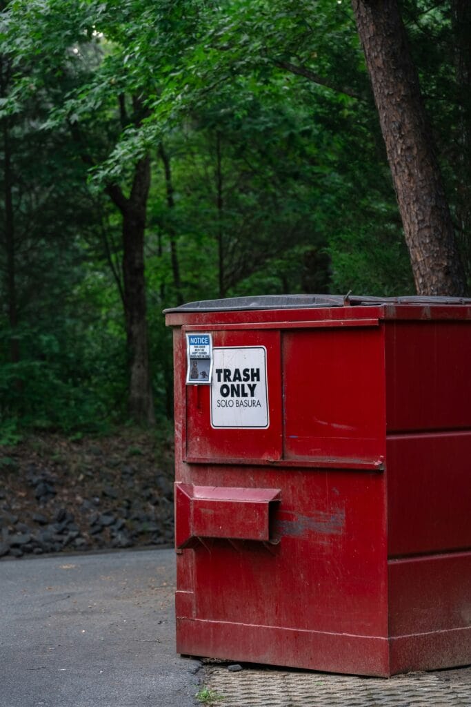 A red commercial dumpster with signs warning "Trash Only" and "Keep Lid Closed."